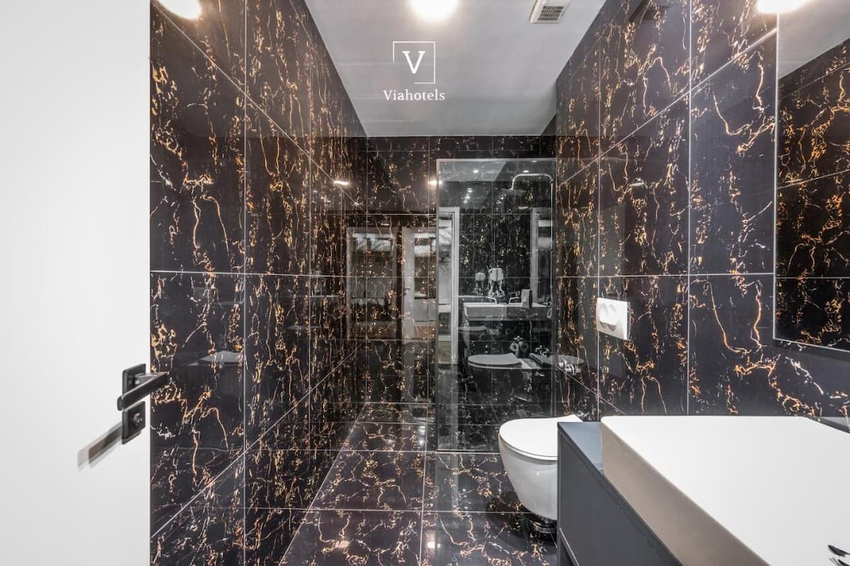 Un baño moderno con baldosas de mármol negro y mampara de cristal.
