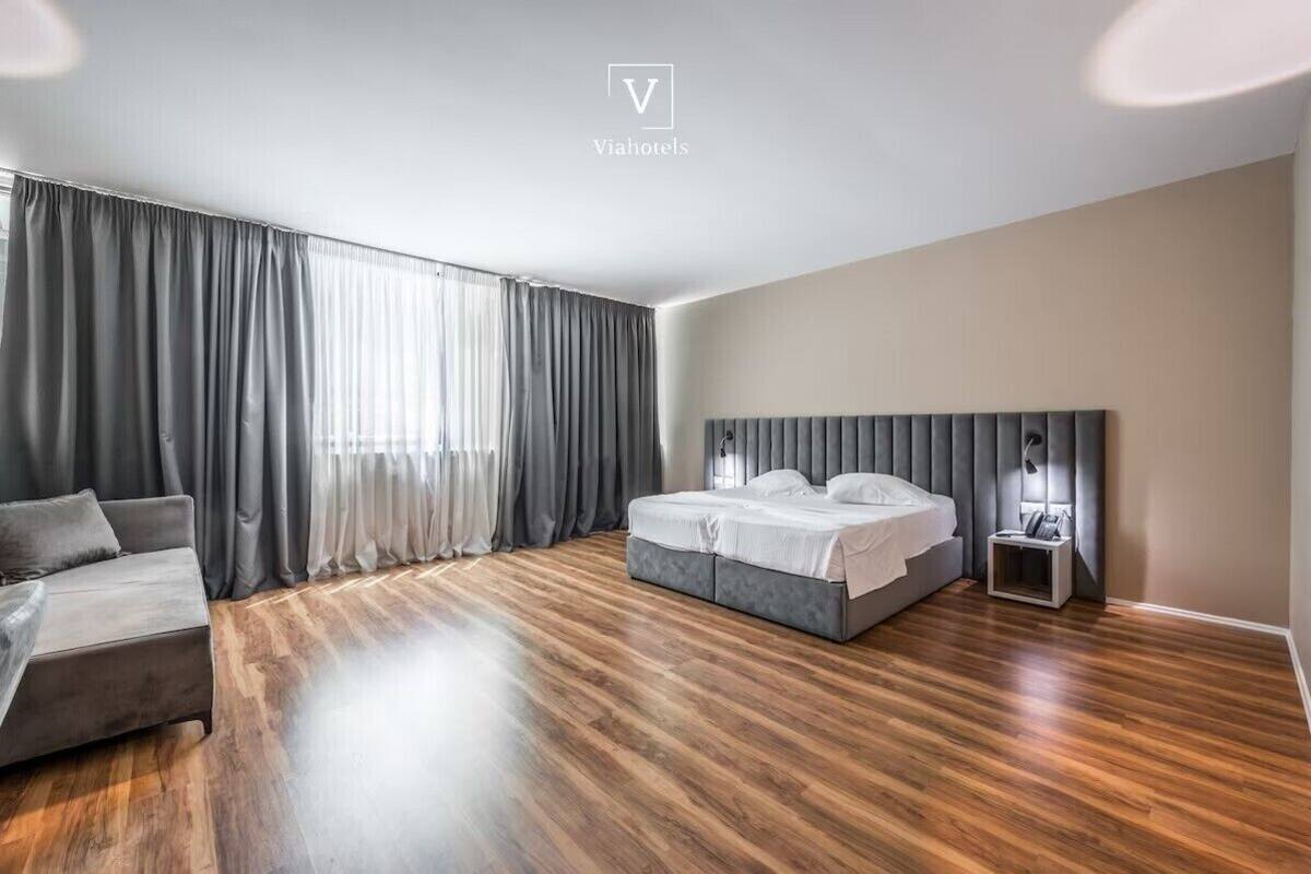 Una habitación de hotel moderna con una cama grande, un sofá y una mesita de noche.