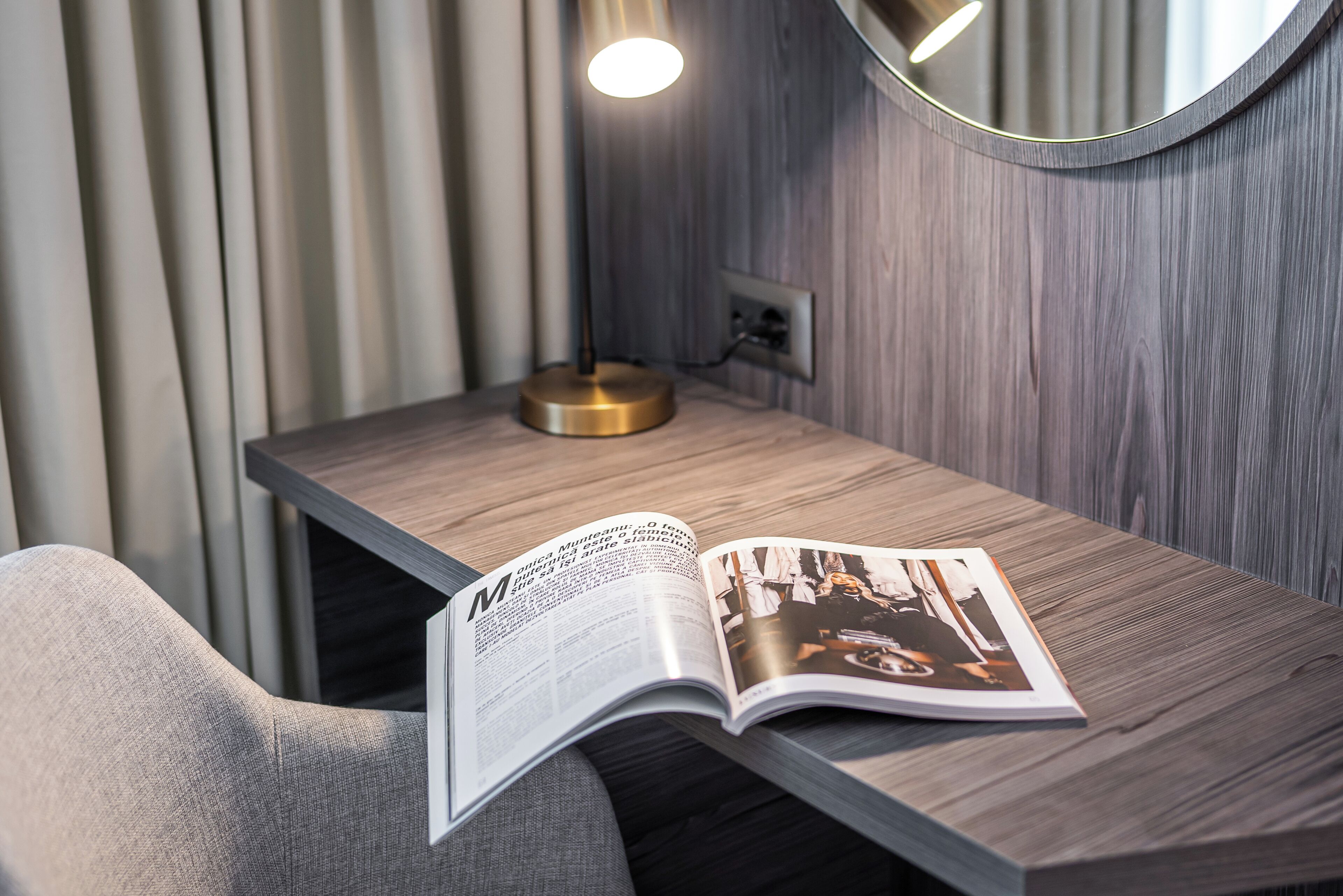 Una habitación moderna con un escritorio de madera, una lámpara y una revista abierta sobre el escritorio.
