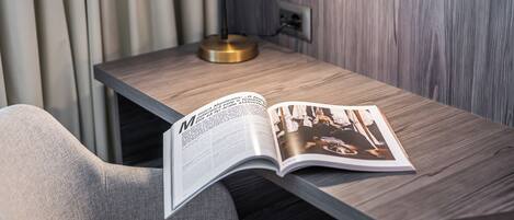 A modern room with a wooden desk, a lamp, and a magazine open on the desk.