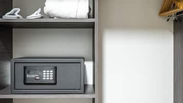 A modern, minimalist closet with a combination lock safe, neatly folded towels, and a hanging rack.