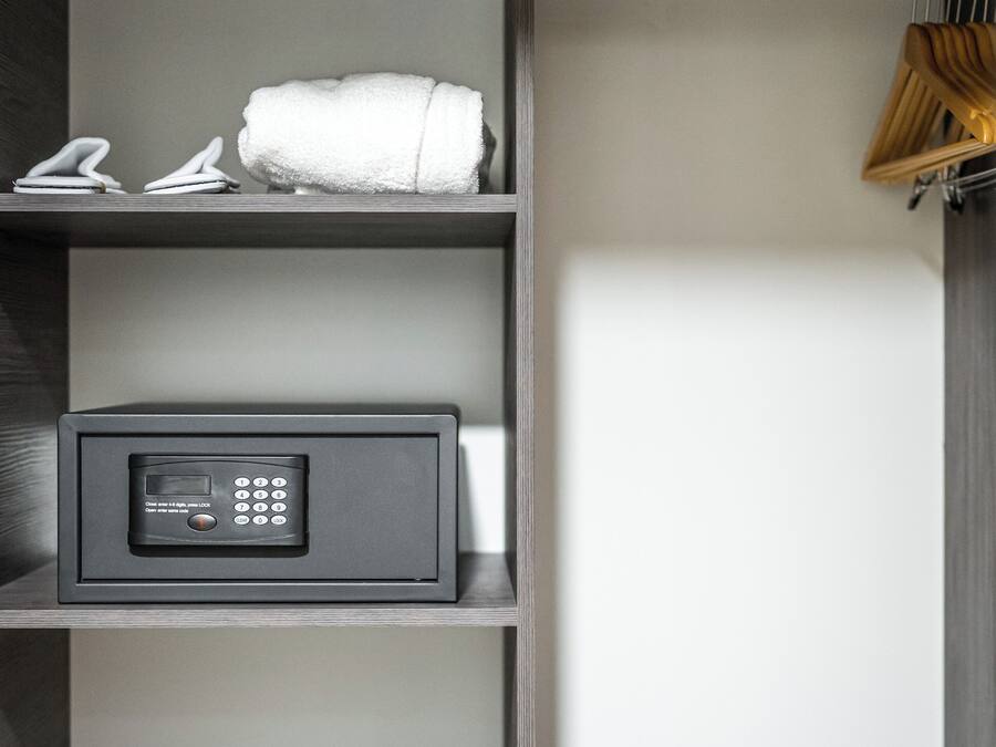 A modern, minimalist closet with a combination lock safe, neatly folded towels, and a hanging rack.