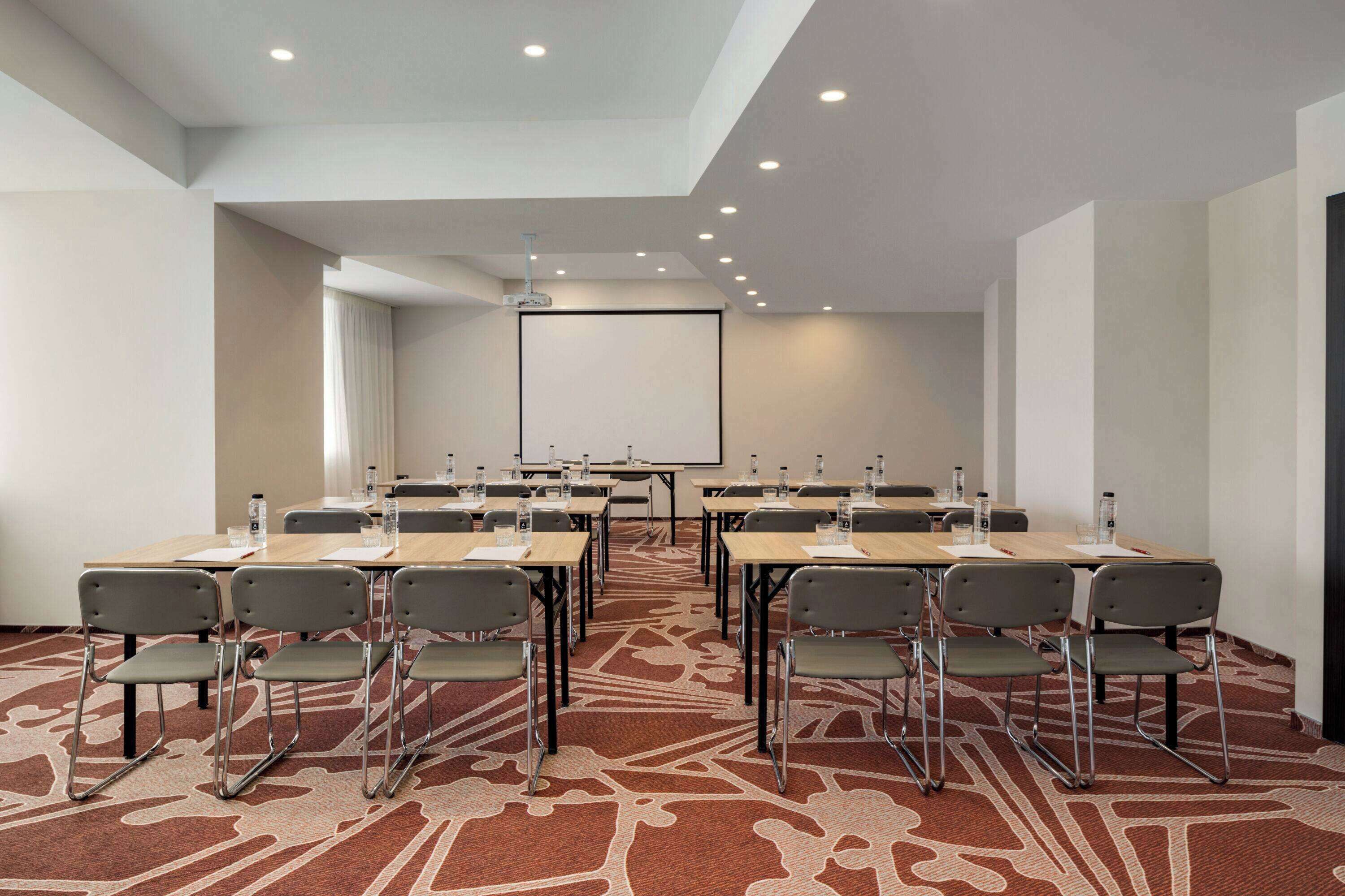A conference room with a large screen, multiple tables, and chairs.