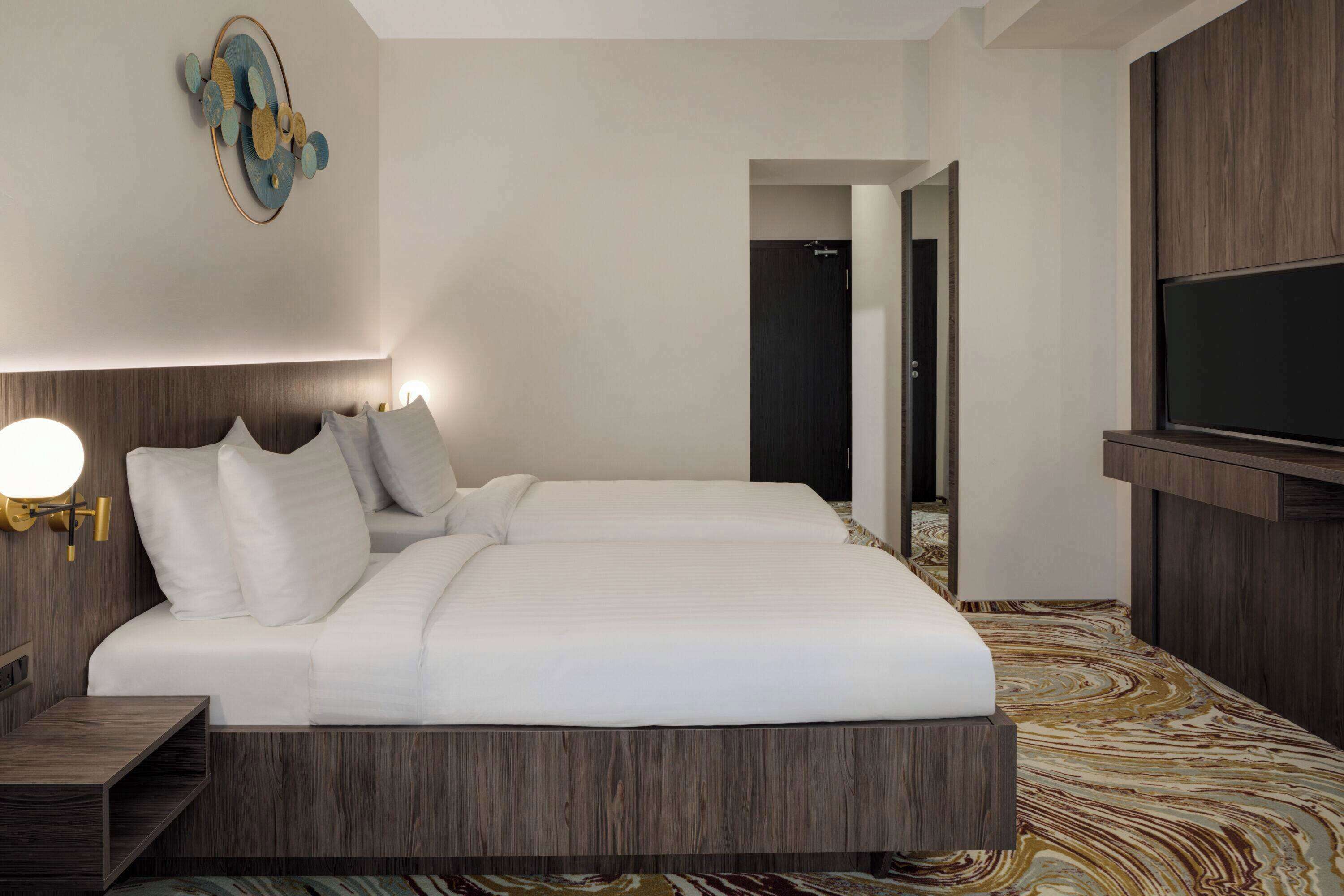 A modern hotel room with a large bed, a TV mounted on the wall, and a wooden headboard.