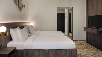 A modern hotel room with a large bed, a TV mounted on the wall, and a wooden headboard.