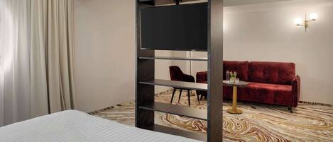Een hotelkamer met een bed, een aan de muur bevestigde televisie, een rode bank, een tafeltje en een kamerbreed tapijt met een patroon.