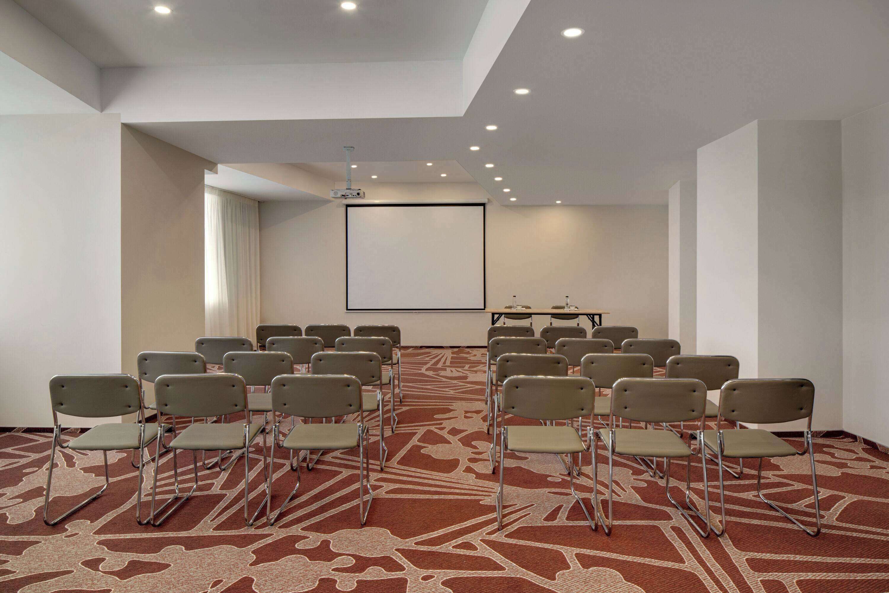 A conference room with rows of chairs, a projector screen, and a carpeted floor.
