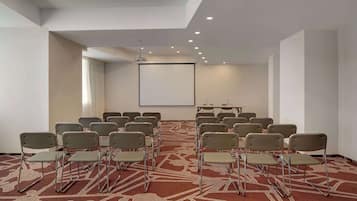 A conference room with rows of chairs, a projector screen, and a carpeted floor.