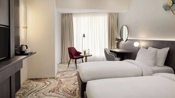 A hotel room with two beds, a desk, a chair, a TV, and a large window with curtains.