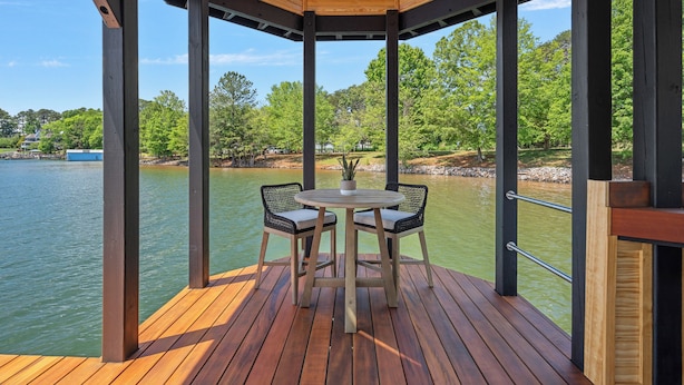 Une terrasse en bois avec une table ronde et deux chaises, donnant sur une étendue d’eau et une zone verdoyante.