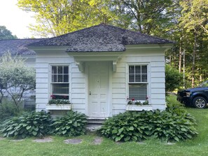 A small, single-story house with a white exterior and a dark roof. It features a front door, two windows with shutters, and a small porch area. - Nightingale Cottage (Mount Vernon)