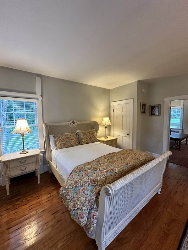 A bedroom with a bed, two bedside tables, a window with blinds, and a door. - Nightingale Cottage (Mount Vernon)