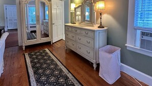 Een kamer met houten vloer, een grote spiegel, een dressoir en een raam met jaloezieën.