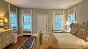 A bedroom with a bed, dresser, and two windows with blinds.