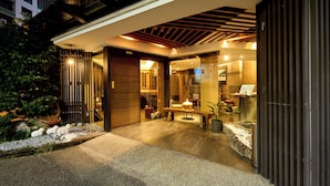 A modern building with a well-lit entrance, a wooden bench, and a small garden area with white pebbles and plants. - Tenlien onsen Hot Spring Hotel (Jiaoxi)