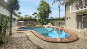 A swimming pool with a brick edge, surrounded by a gravel area and palm trees.