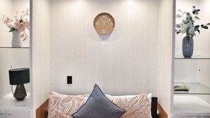 A bedroom with a bed, a wall clock, a nightstand with a lamp, and two vases with flowers.