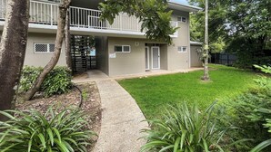 A two-story building with a balcony, a gated entrance, and a well-maintained lawn.