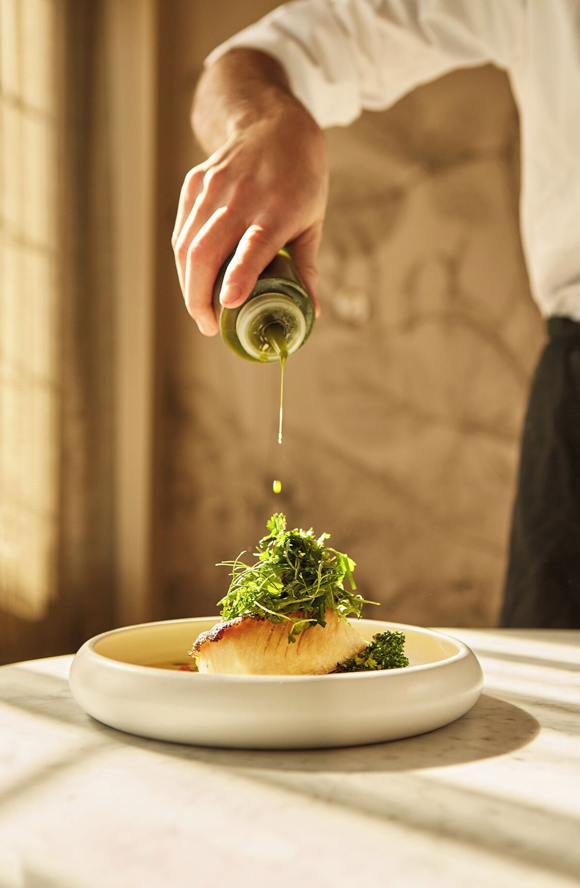 Un chef vertiendo aceite sobre un plato con pescado y verduras.