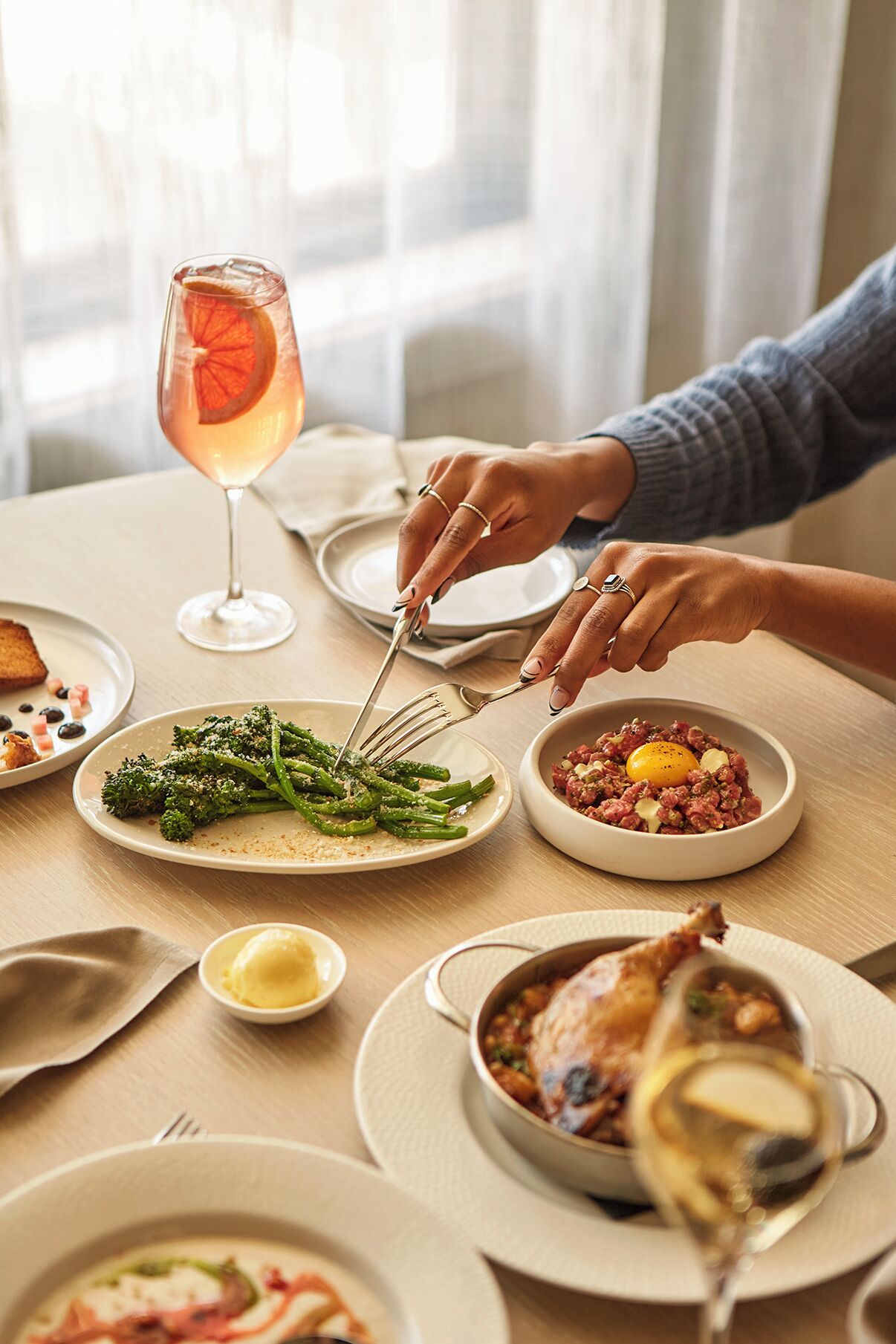 Une table à manger avec différents plats, notamment un verre d’une boisson rose, une assiette d’asperges et un bol de viande avec un œuf.