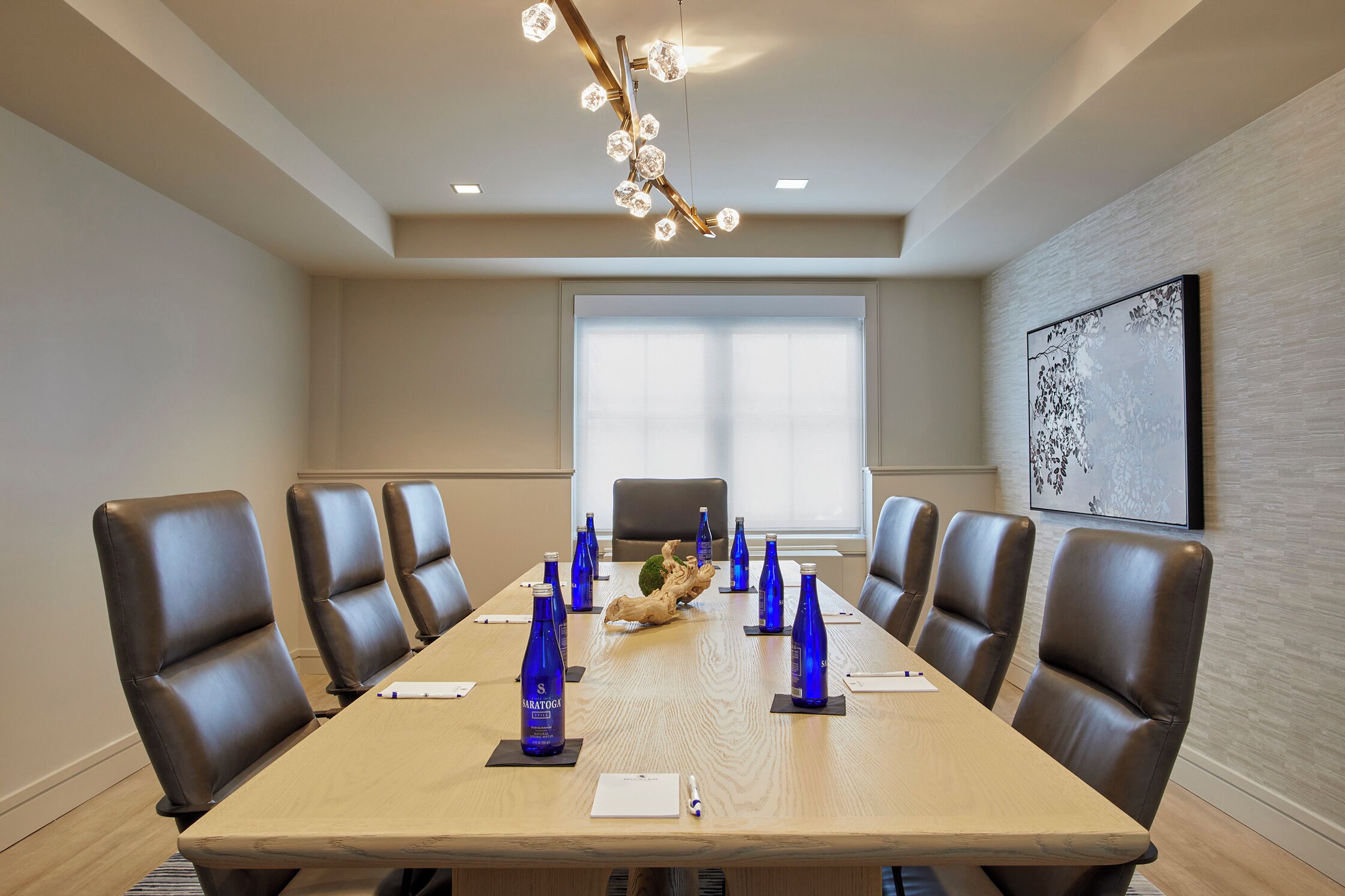 A conference room with a long table, brown leather chairs, and a chandelier.