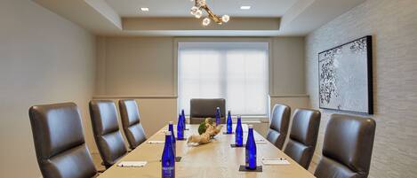 A conference room with a long table, brown leather chairs, and a chandelier.