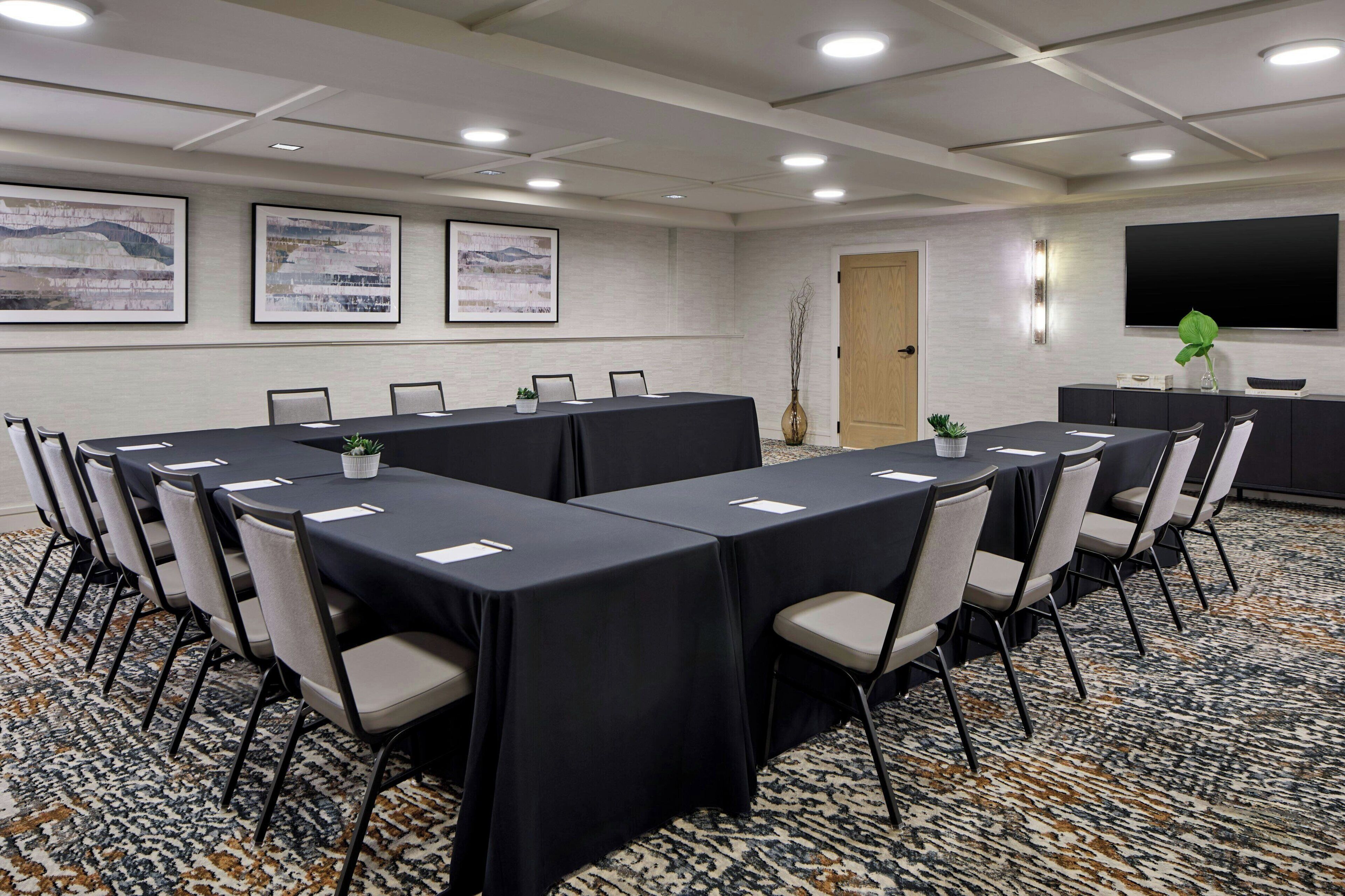 A conference room with a long table, chairs, a TV, and framed artwork on the wall.