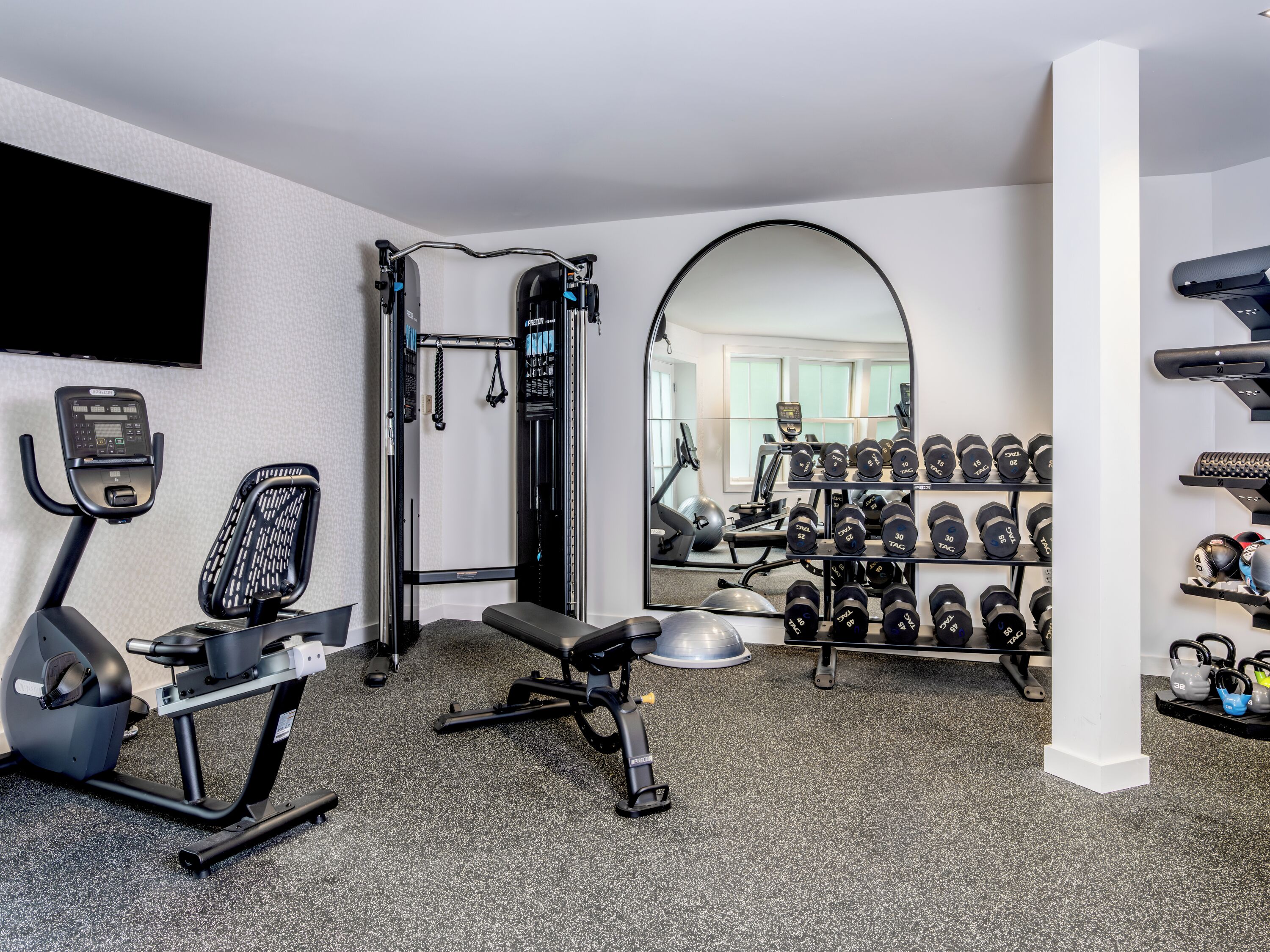 A home gym with a treadmill, exercise bike, bench, weight rack, and mirror.