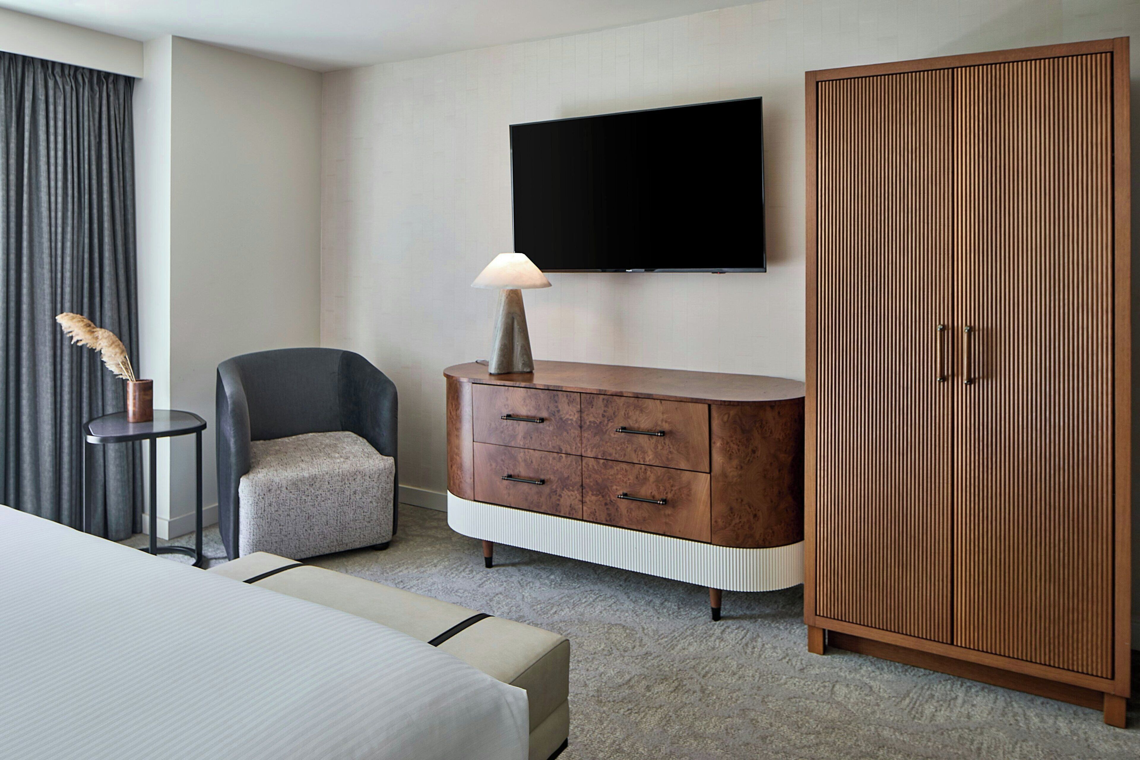 Una habitación de hotel con cama, escritorio, silla, televisor y armario.