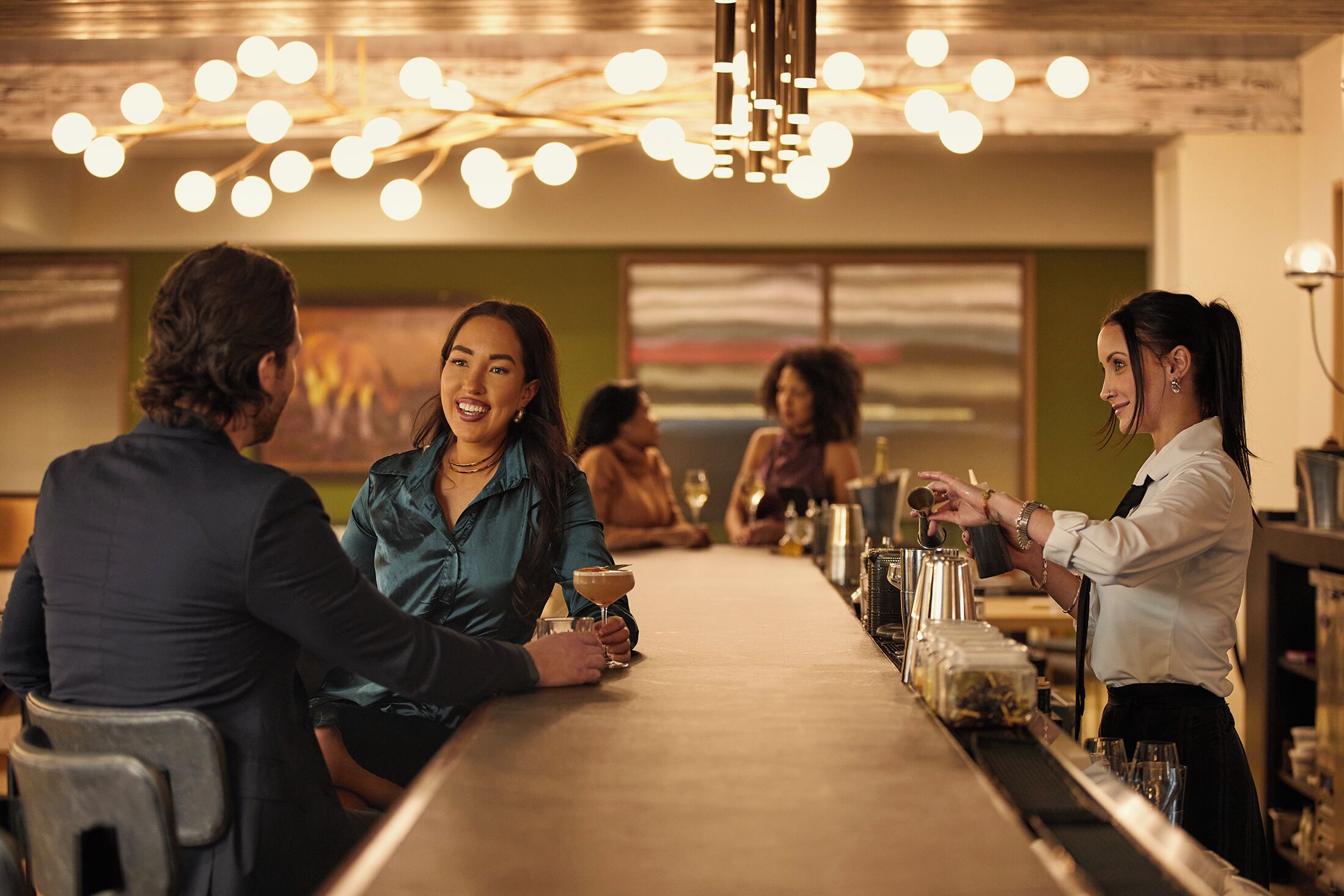 A bar area with a long counter, bar stools, and a bartender serving drinks.