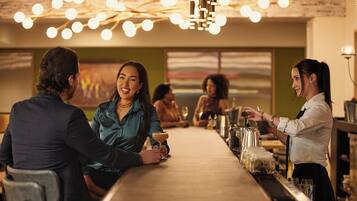 A bar area with a long counter, bar stools, and a bartender serving drinks.