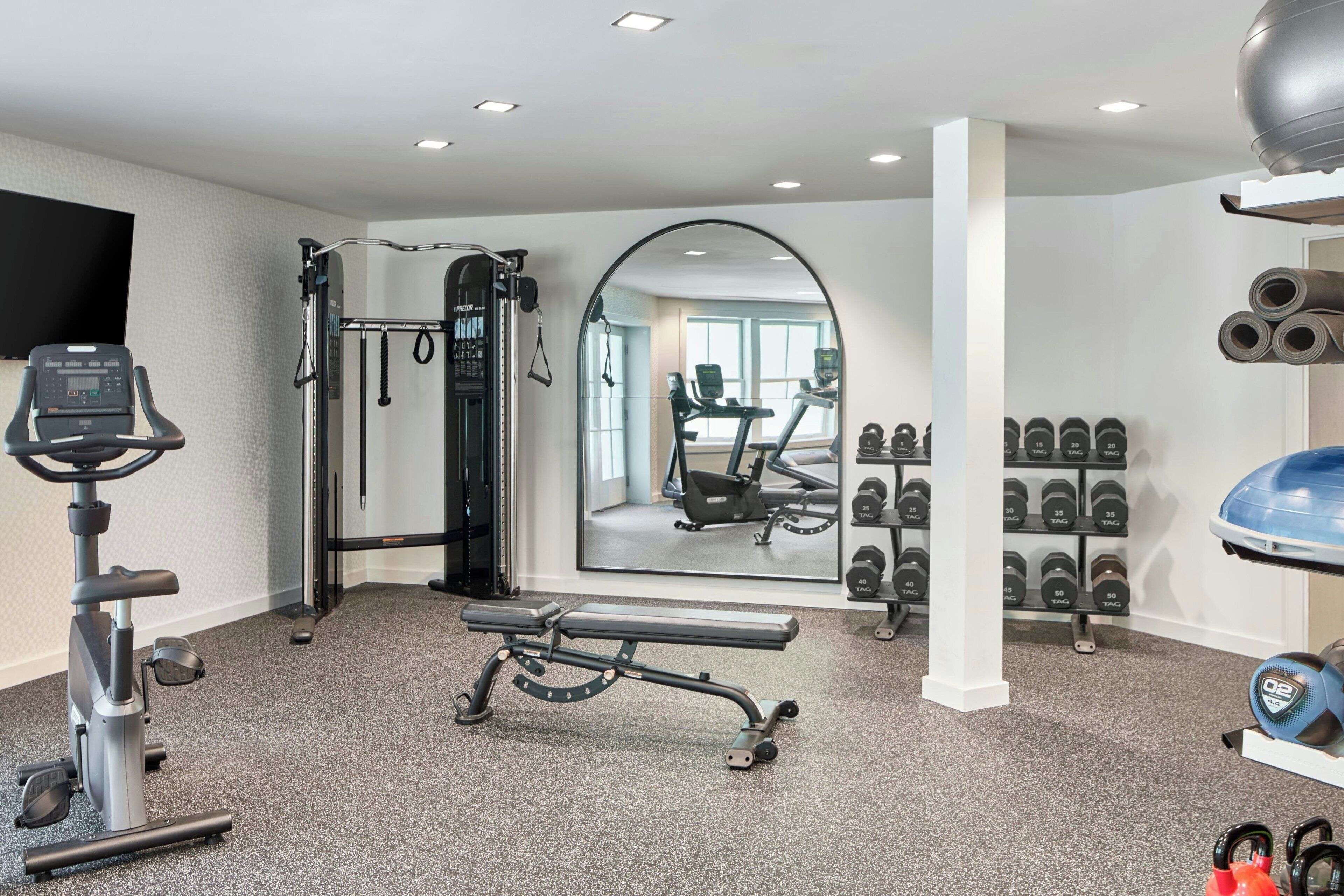 Een fitnessruimte met trainingsapparatuur, een spiegel en gewichtrekken.