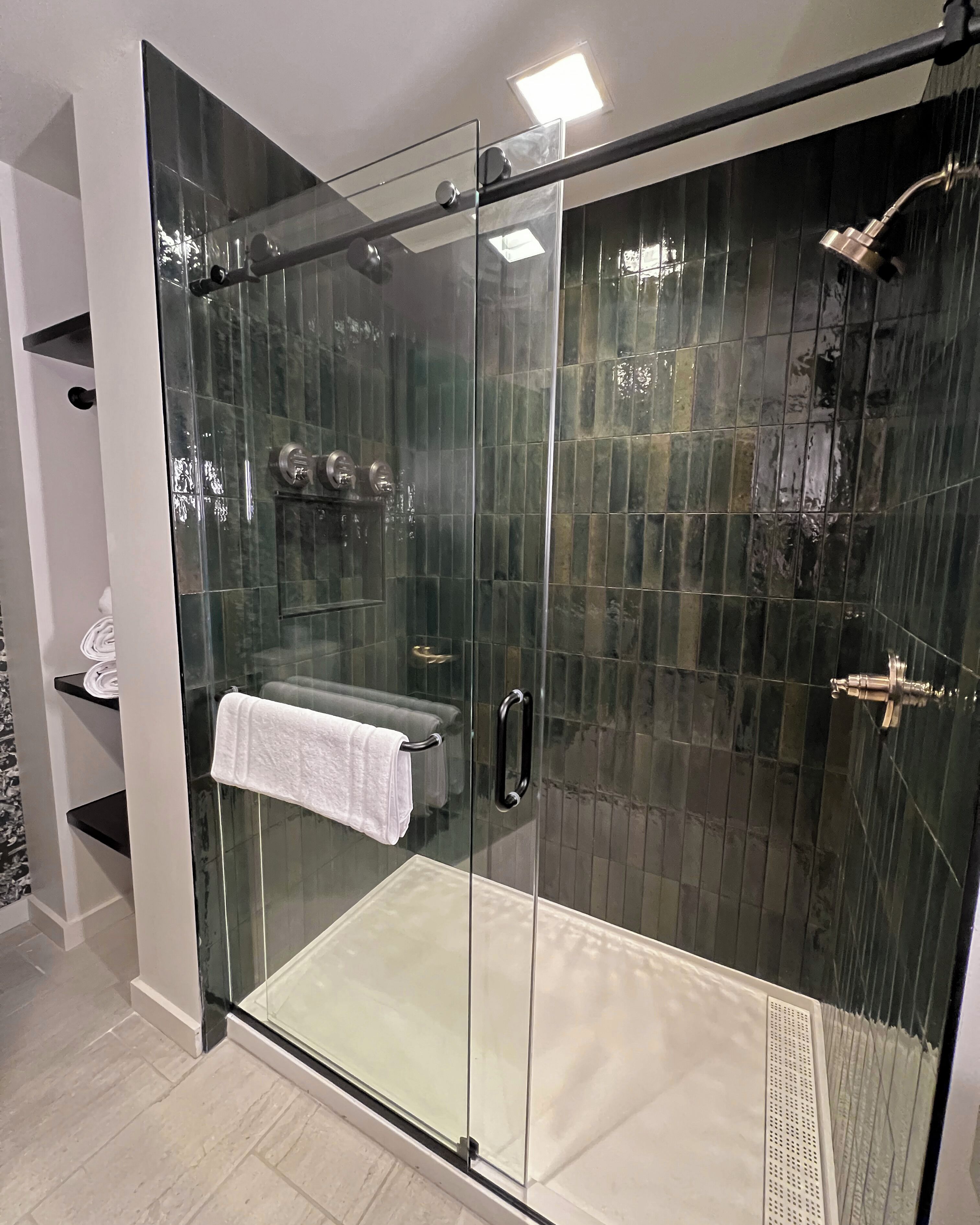 A modern bathroom with a glass-enclosed shower, a white towel on the door, and a tiled floor.