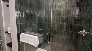 A modern bathroom with a glass-enclosed shower, a white towel on the door, and a tiled floor.