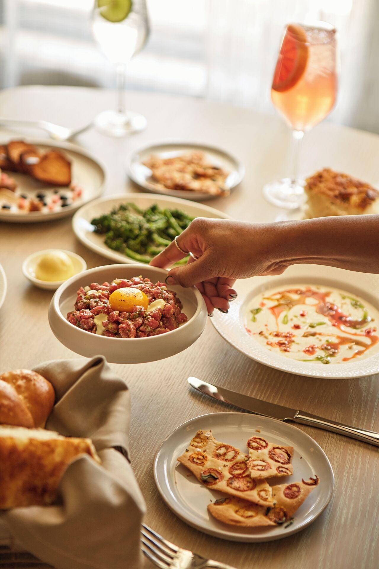 Una mesa de comedor con varios platos, incluyendo un tazón de ensalada de carne, un plato de verduras verdes y una porción de pizza.