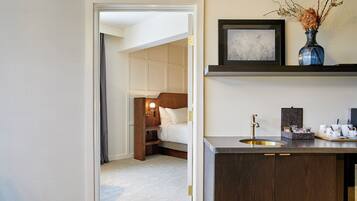 A hotel room with a bed, a bedside table, a nightstand, a built-in shelf, a sink, and a mirror.