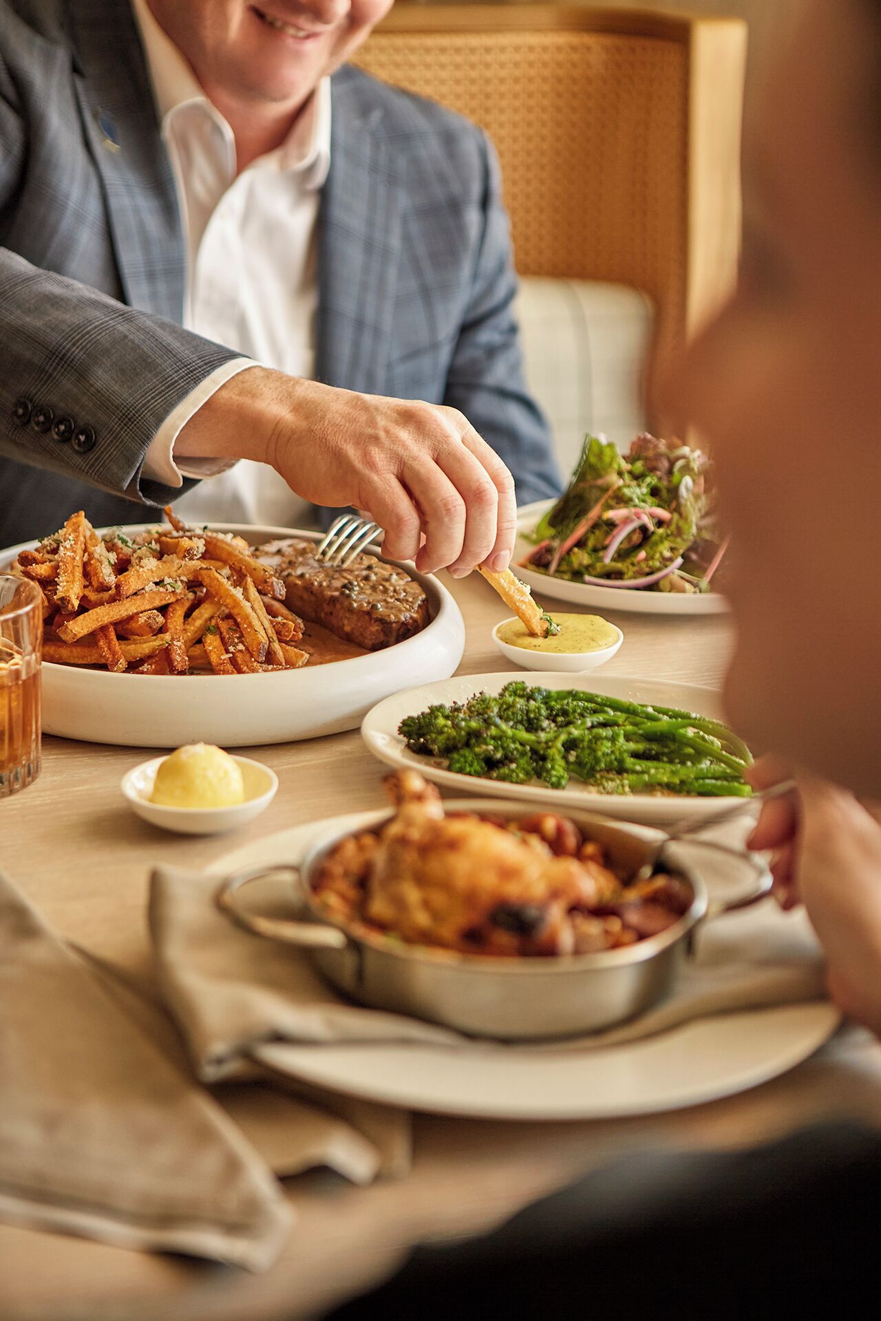 Una mesa de comedor con diferentes platos, como un bistec, papas fritas y verduras.