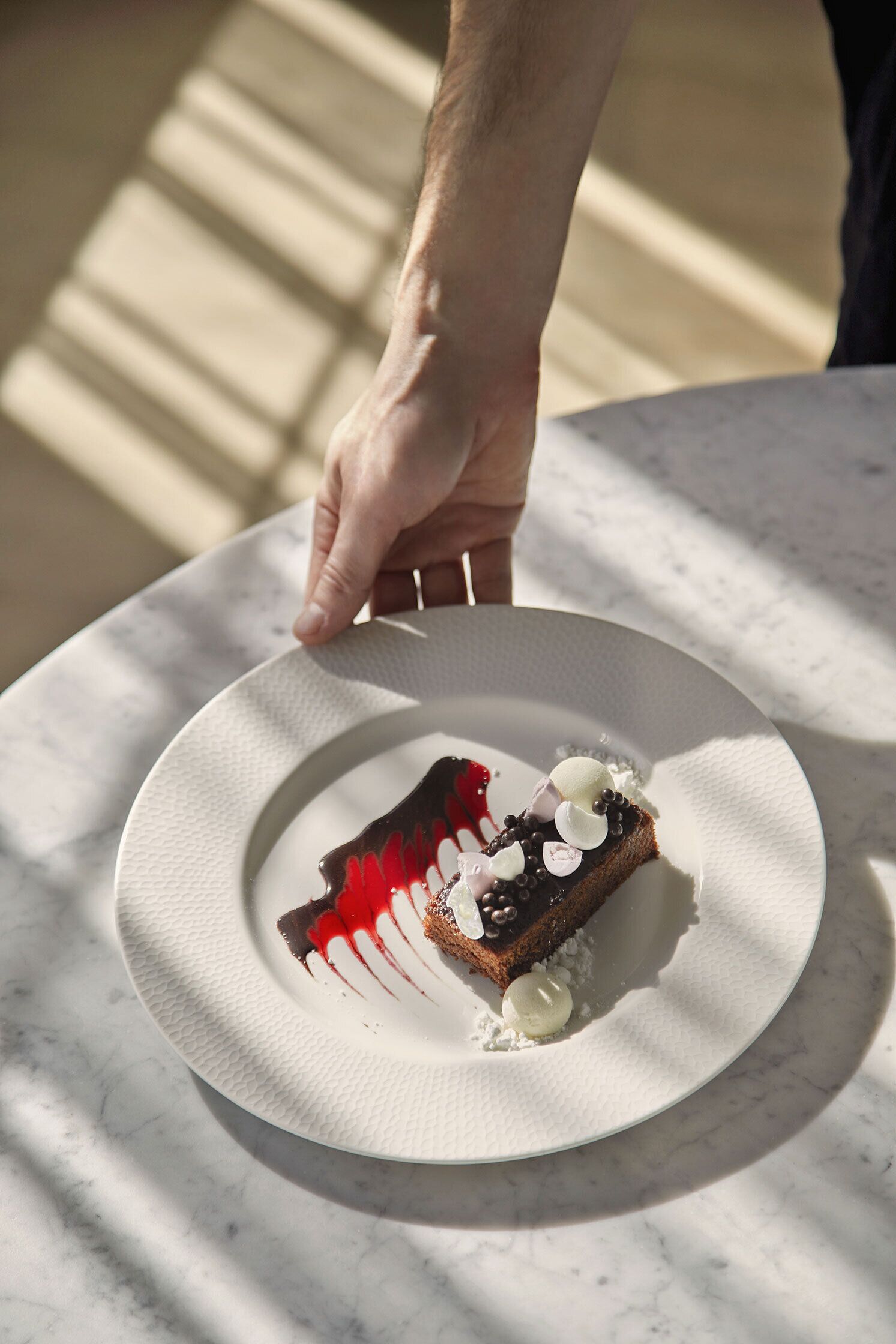 A dessert on a white plate with a hand reaching for it.