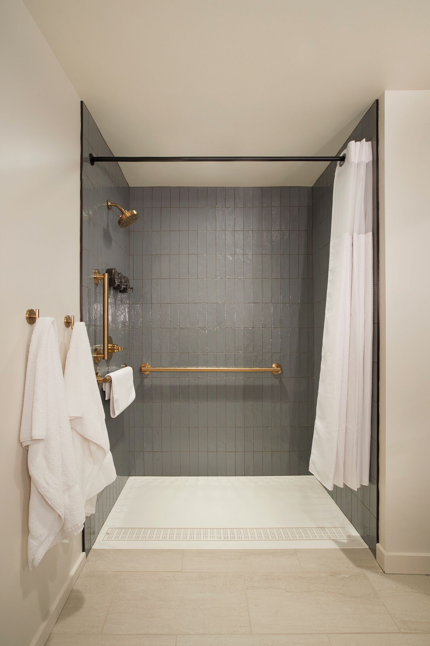 A modern bathroom with a glass shower enclosure, a gold showerhead, and a white towel rack.