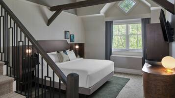 Un dormitorio con cama, mesita de noche, televisor, ventana con cortinas, escalera y tragaluz.