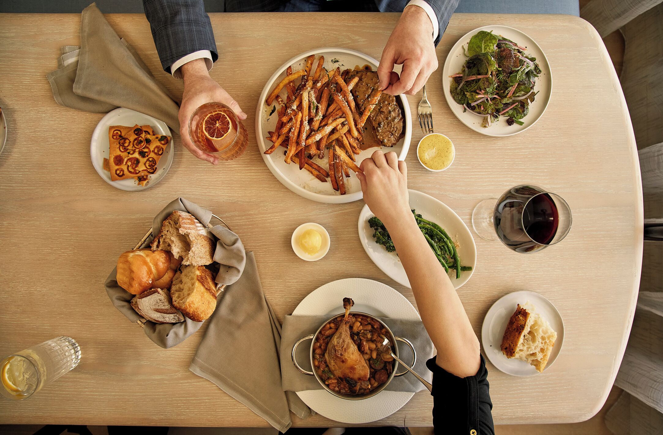 Una mesa de comedor con diversos platos, incluyendo papas fritas, carne, ensalada y pan.