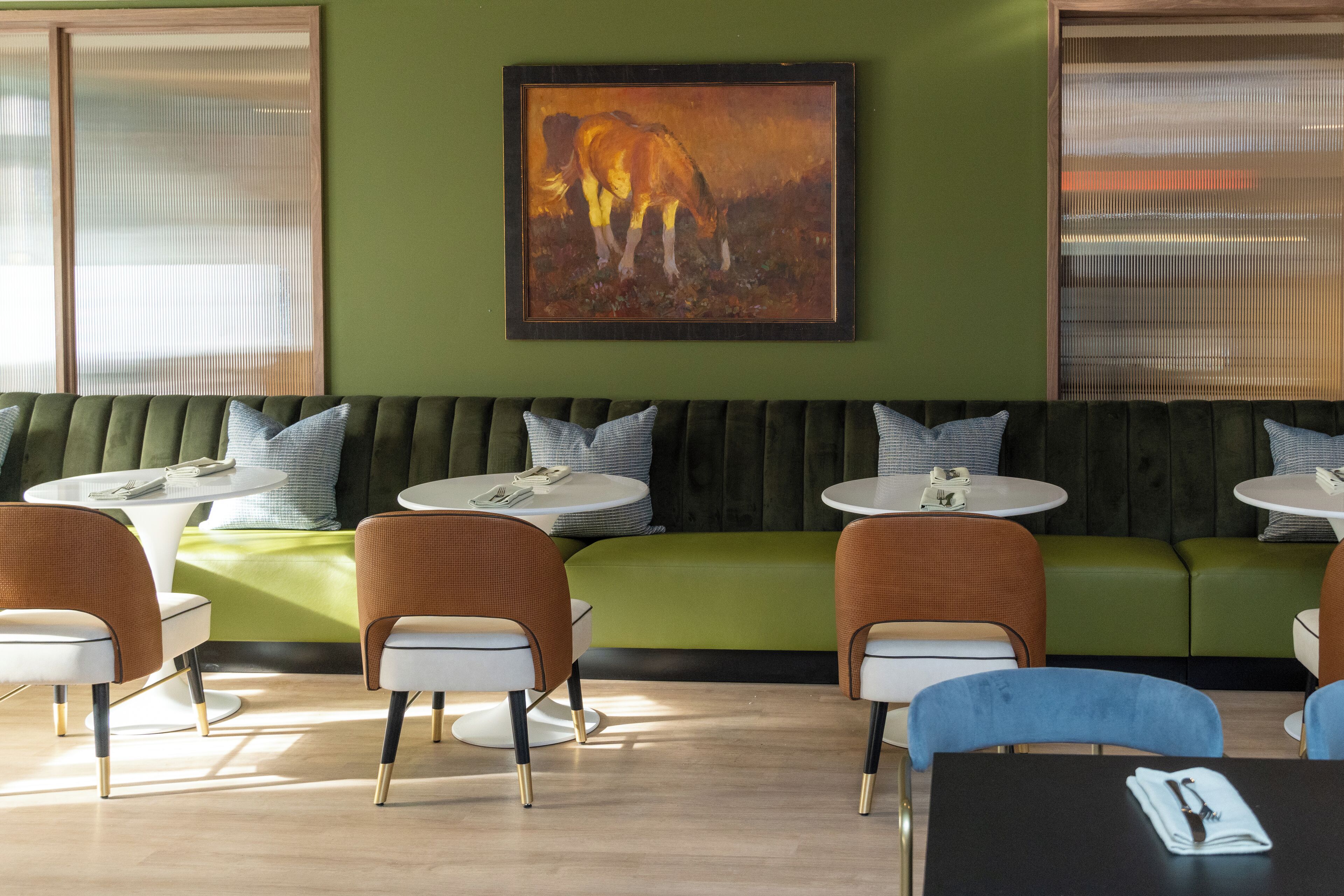 Ett modernt loungeområde med en grön soffa, vita, runda bord och orangefärgade stolar.