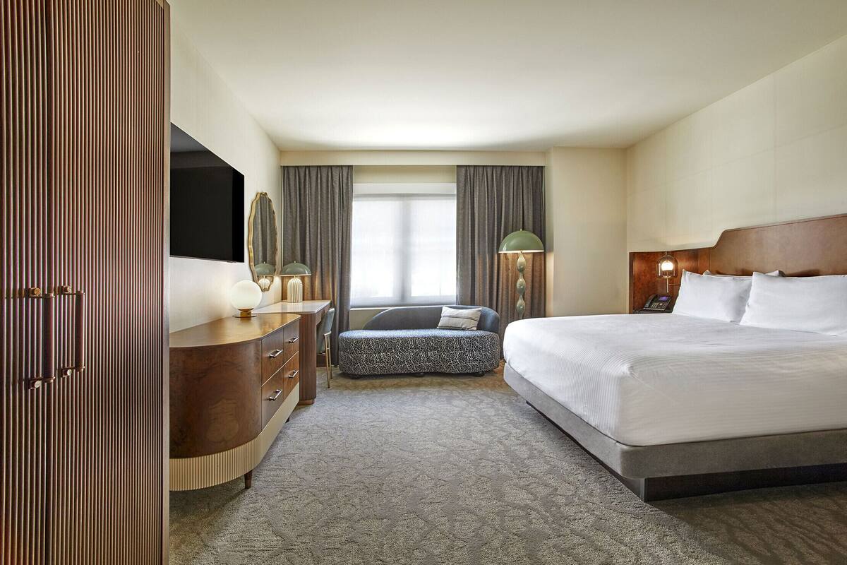 A hotel room with a bed, a sofa, a desk with a lamp, and a wardrobe.