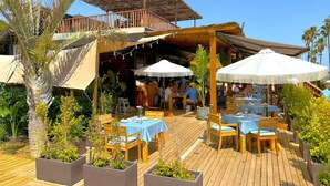 Een terras met houten tafels en stoelen, omgeven door plantenpotten en parasols.