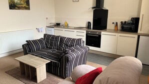 A living room with a striped sofa, a beige sofa, a coffee table, and a kitchen area with appliances. - Charlotte Street (Ayr)