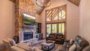 A cozy living room with a stone fireplace, leather sofas, and a large window with a view of greenery. - On Mountain Time at Eagles Nest - single level w/hot tub, views, firepit (Banner Elk)
