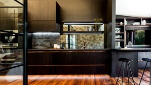 A modern kitchen with dark cabinetry, a stone backsplash, and a wooden floor.