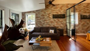 A modern living room with a brick wall, a brown leather sofa, a wooden coffee table, and a ceiling fan.