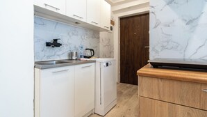 A compact kitchen with white cabinets, a marble backsplash, a built-in dishwasher, and a wooden countertop.