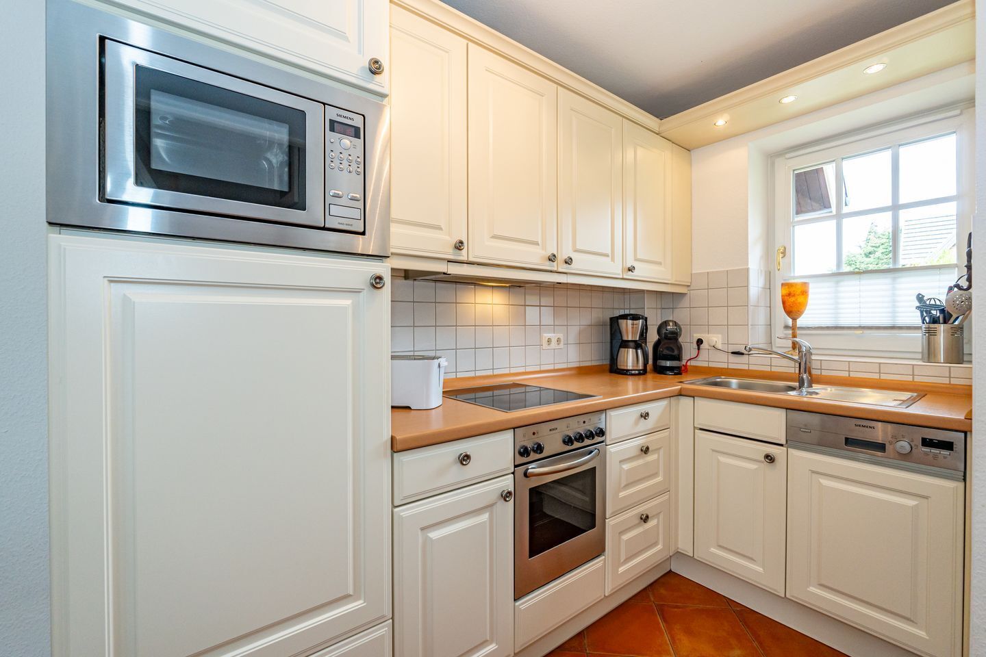 Una cocina moderna con armarios blancos, electrodomésticos de acero inoxidable y un ventanal que proporciona luz natural.